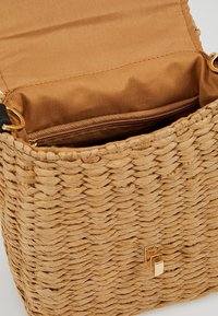 Borsa intrecciata in paglia con interni in tessuto beige, tasca con zip e un accessorio in metallo color oro sulla parte anteriore.