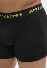 Boxer noirs avec une ceinture élastique jaune marquée. Le tissu semble lisse avec une coupe ajustée et des détails de couture renforcée.