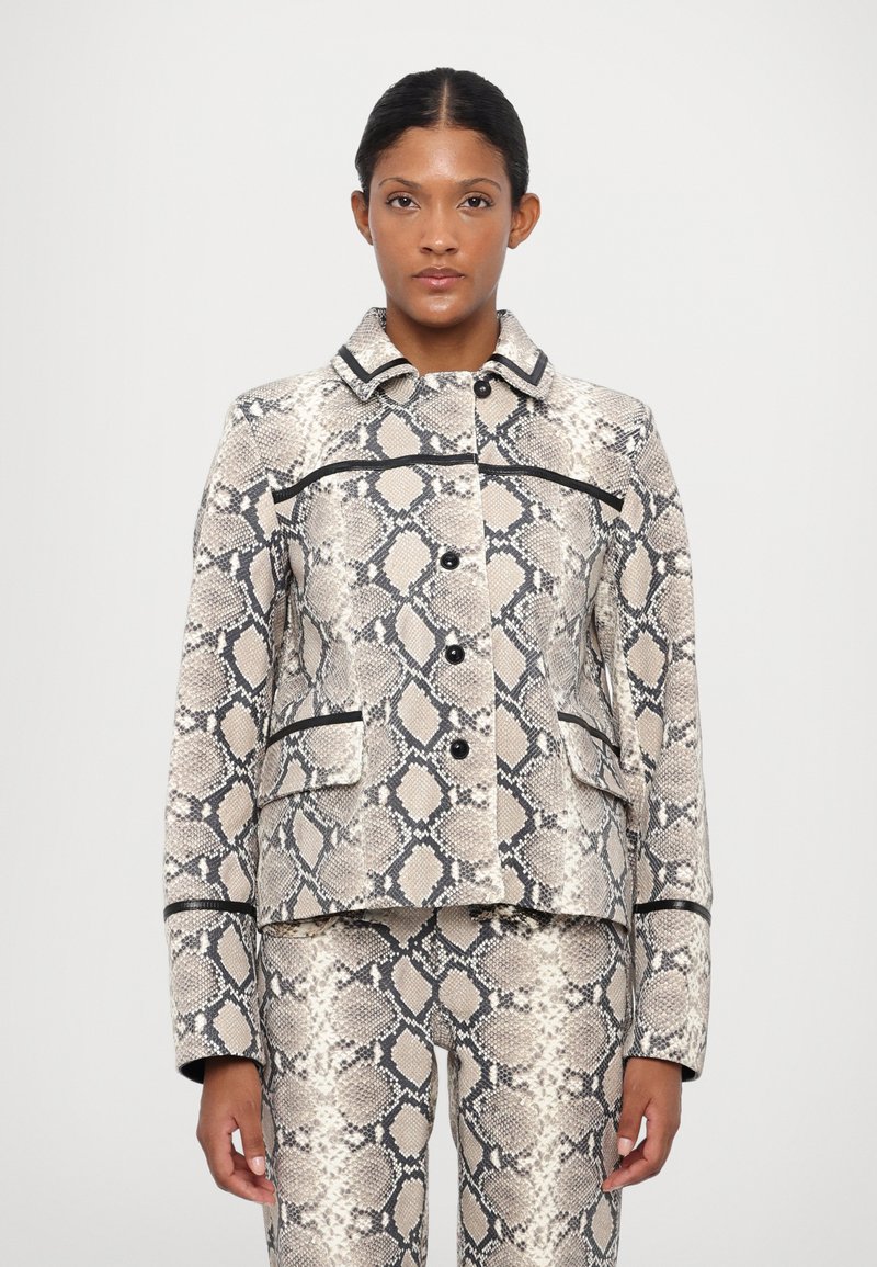 Chaqueta de estampado de serpiente en tonos beige y negro, con cuello con solapa, botones frontales y dos bolsillos. Presenta un ribete negro a lo largo de las costuras.
