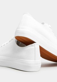 Vita canvas sneakers med en strukturerad överdel, platt vit gummisula och gummigummikontakt. Har en låg design och platta skosnören.