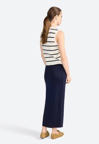 Top senza maniche a righe color crema abbinato a una gonna maxi blu navy unita; tessuto leggero, silhouette aderente, texture liscia, con spacco laterale.