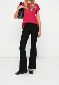 Svarta utsvängda byxor kombinerade med en fuchsia kortärmad topp. Toppen har en avrundad passform och en mjuk textur, och outfiten kompletteras av en svart väska.