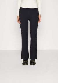 Marineblauwe geribde flared pants met een aansluitende tailleband, gecombineerd met zwarte schoenen met dikke zolen; minimalistisch ontwerp met een gladde textuur.