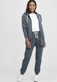 Grå hettegensere med hvite snorer, kombinert med matchende joggebukser med snor i livet og hvite sidelister.