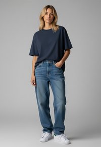 Marineblaues, oversized T-Shirt mit kurzen Ärmeln, kombiniert mit hellblauen, geraden Jeans und weißen Sneakern, minimalistisches Design ohne Muster.