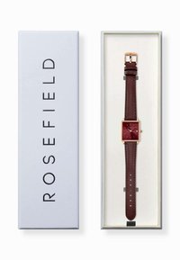 Montre carrée avec un cadran bordeaux, des accents dorés et un bracelet en cuir brun dans une boîte blanche avec "ROSEFIELD" imprimé sur le côté.