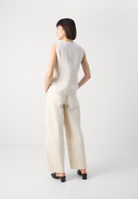 Lichtbeige mouwloze top met een relaxte pasvorm, gecombineerd met crèmekleurige wijde broekspijpen en zwarte muiltjes. Gladde stof, minimalistisch design.