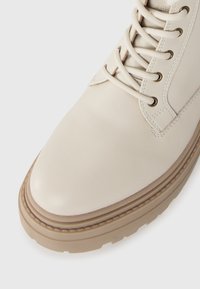 Bota de caminhada em couro creme com biqueira arredondada, design de atacadores, ilhós de metal e sola de borracha bege contrastante.