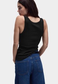 Débardeur noir côtelé avec un col rond et une coupe ajustée, associé à un jean en denim bleu taille haute avec poches arrière.