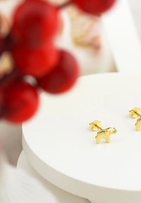 Guld elefantformade studörhängen med en glänsande yta, monterade på en cirkulär vit display. Små stjärnformade baksidor är synliga.