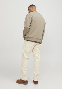 Beige sweatshirt, cream pants, and brown shoes. Sweatshirt features a round neck and ribbed cuffs. Pants have back pockets and a straight fit.