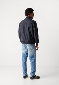 Marine bomberjakke med ribbede manchetter, parret med lyseblå denim jeans og sorte sneakers med hvide striber. Neutral baggrund.