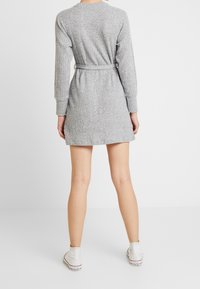 Harmaa ribatetun mekko pitkilla hihoilla, vyötaiteella ja polven ylle ulottuvalla pituudella. Yhdistetty valkoisten lenkkareiden kanssa, siinä on teksturoitu kangas.