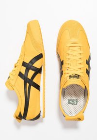 Yellow leather sneakers with black accents, round toe, textured suede on the upper, flat laces, and perforated insole.