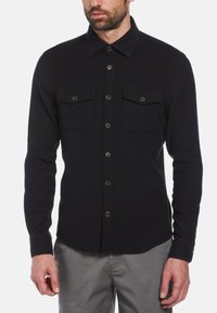 Zwart longsleeve shirt gemaakt van stof met een gladde textuur, voorzien van twee borstzakken, knoopsluiting en een klassieke kraag.
