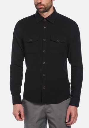 Zwart longsleeve shirt gemaakt van stof met een gladde textuur, voorzien van twee borstzakken, knoopsluiting en een klassieke kraag.