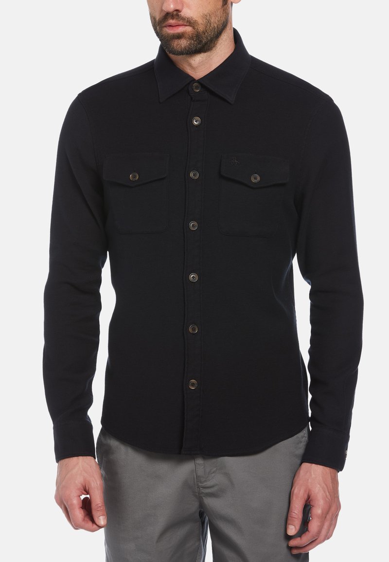 Zwart longsleeve shirt gemaakt van stof met een gladde textuur, voorzien van twee borstzakken, knoopsluiting en een klassieke kraag.