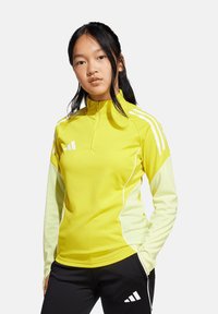 Geel sporttop met kwart-rits kraag, lange mouwen in een lichter geel, witte accenten en een aansluitend ontwerp. Zwarte broek met logodetail.