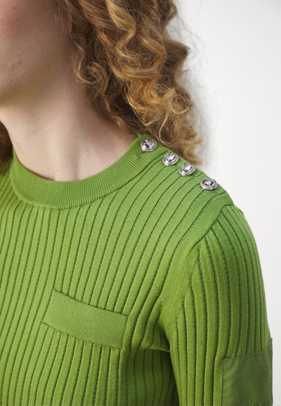 Grüner gerippter Strickpullover mit Rundhalsausschnitt, ausgestattet mit einer Brusttasche und vier metallischen Knöpfen auf der linken Schulter.