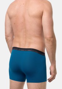 Pánské tyrkysové boxerky s černým elastickým pasem se značkou. Materiál je hladký a střih padne na tělo.