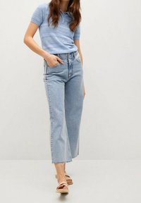 Polo-shirt en tricot bleu clair à manches courtes, associé à un jean en denim clair taille haute et ample avec un ourlet effiloché, complété par des sandales beiges.