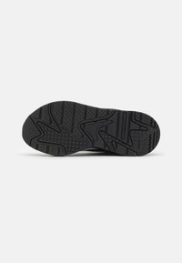 Semelle de sneaker noire avec motif de grip texturé comportant des rainures, des points et des formes angulaires pour la traction.