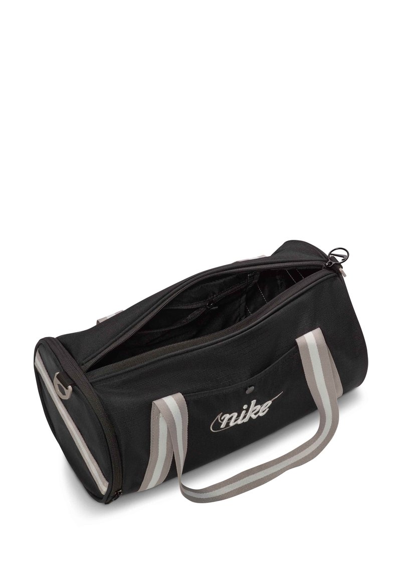Bolsa de viaje de tela negra con asas a rayas grises, cierre de cremallera y el logo de Nike prominentemente mostrado en un lado.