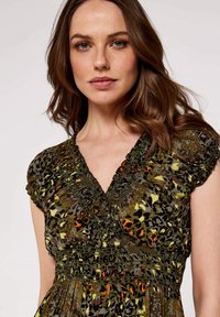 Blumenkleid mit Tiermuster, das geraffte Schultern, einen tiefen V-Ausschnitt und eine smockierte Taille aufweist. Die dominierenden Farben sind Grün, Schwarz, Gelb und Orange.