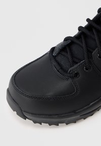 Shoe preto para exterior com um upper de couro liso, detalhes em tecido texturizado e uma sola de borracha robusta com padrão de tracção visível.