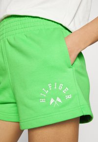 Pantalones cortos de algodón verdes con una cinturilla elástica, que presentan el texto blanco "HILFIGER" y gráficos de bandera en el lado inferior izquierdo.