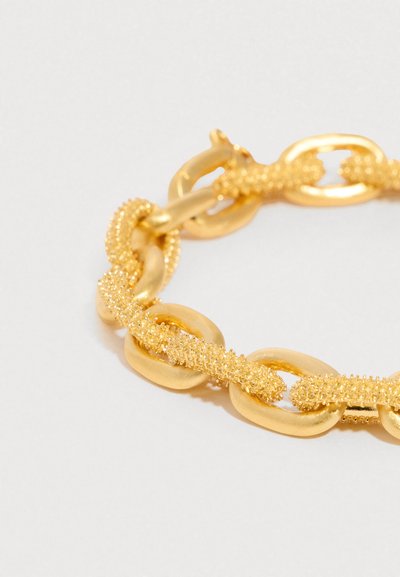 Arany karkötő nagy, sima, ovális láncszemekkel, melyek texturált, gyöngyszerű arany láncokkal vannak összefonódva, fehér háttéren.