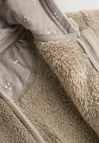 Hellbrauner Fleece-Stoff mit einer weichen, flauschigen Textur; beinhaltet ein gemustertes Innenfutter und einen glatten Rand entlang der Kanten.