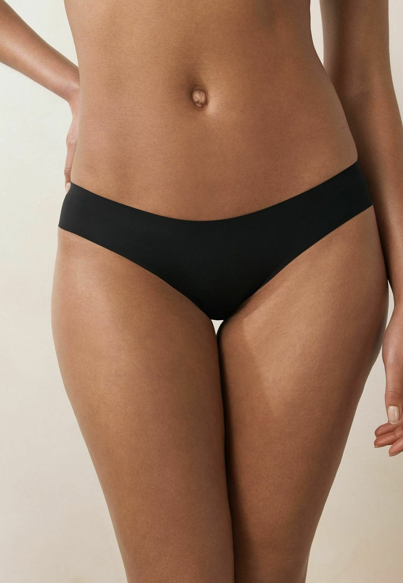 Czarne bikini z gładkiego, miękkiego materiału. Skrojone w niskim kroju, z minimalnym zakryciem, z bezszwowymi brzegami i bez widocznych elementów metalowych.