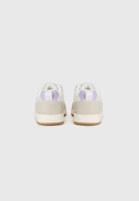 Baskets blanches avec des accents en daim gris clair, présentant une bande violette au niveau du talon, un bout arrondi et une semelle en caoutchouc texturée.