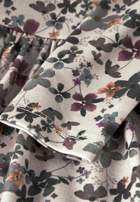 Lillede mustriga kangas vaigistatud halli, lilla ja oranži tooni. Pehme tekstuur pleeditud detailide ja nähtava õmblusega ääres.