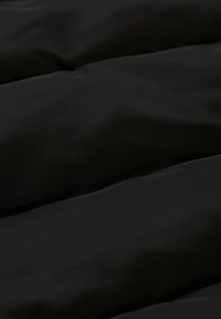 Schwarzer gepolsterter Stoff mit einer glatten Textur und dezentem Glanz sowie horizontalen Steppnähten, die Weichheit und Isolierung betonen.