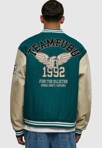 Jachetă de tip varsity în nuanțe de teal și crem, cu broderia "TEAMFUBU" și "1992" pe spate, având manșete și talie ribbate.