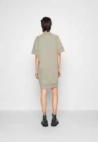 Oversized oliwkowa sukienka-sweterek z krótkimi rękawami, z prążkowanym dołem i minimalnym logo z tyłu. Połączona z czarnymi botkami na platformie.