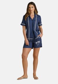 Navyblauwe set met short-sleeve shirt en shorts, versierd met witte geborduurde patronen en een palmenontwerp, gemaakt van een gladde stof.