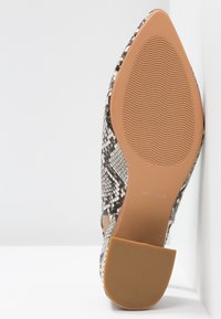 Chaussure à bout pointu avec un motif en peau de serpent, semelle beige avec des lignes ondulées antidérapantes et petit talon carré reposant sur une surface blanche.