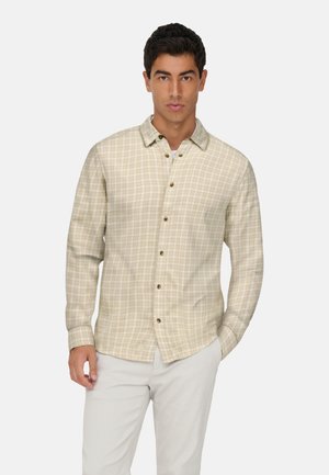 Beige ternet skjorte med lange ærmer, en knappet krave og træknapper. Stoffet har en glat tekstur og er båret over en hvid undertrøje.