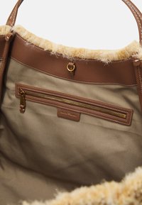 Brun tygkasse med mjuk, fluffig beige kant upptill. Har en ytterficka med dragkedja i guld och läderdetaljer inuti.