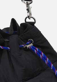Czarna torba materiałowa z zebranym wierzchem, z niebieskimi i czerwonymi sznureczkami oraz srebrnymi elementami, w tym hakiem i oczkiem.