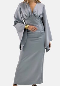 Lange, nauwsluitende jurk van lichtgrijze satijn met een diep V-hals, geplooide taille en brede, vloeiende mouwen. Heeft een gestroomlijnde silhouet en minimale details.