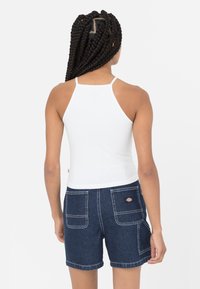Hvit halterneck topp med tynne stropper, kombinert med denimshorts med baklommer og kontraststing. Bakfra vises detaljene på stroppene.