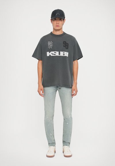 Grijze oversized t-shirt met zwarte graphics, denim jeans en crèmekleurige sneakers. Casual look met een gestructureerde zwarte pet. Minimalistisch design.