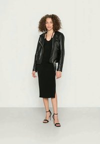 Casaco de motociclista em couro preto, top preto, e saia justa preta até ao joelho, combinados com sandálias de salto alto pretas com tiras.