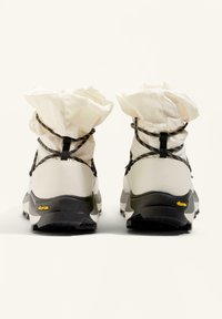 Bílé turistické boty s texturovaným, flexibilním svrškem a elastickými manžetami. Černé kovové prvky a logo Vibram na podrážce.
