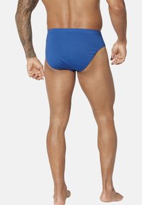 Herren Badebriefe in Blau aus glattem Material, mit einem schlichten Design, tief sitzendem Bund und enge Passform, die die Beindefinition betont.