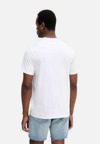 Camiseta de algodón blanca con escote redondo y mangas cortas, vista desde la parte de atrás, combinada con pantalones cortos de mezclilla azul claro.